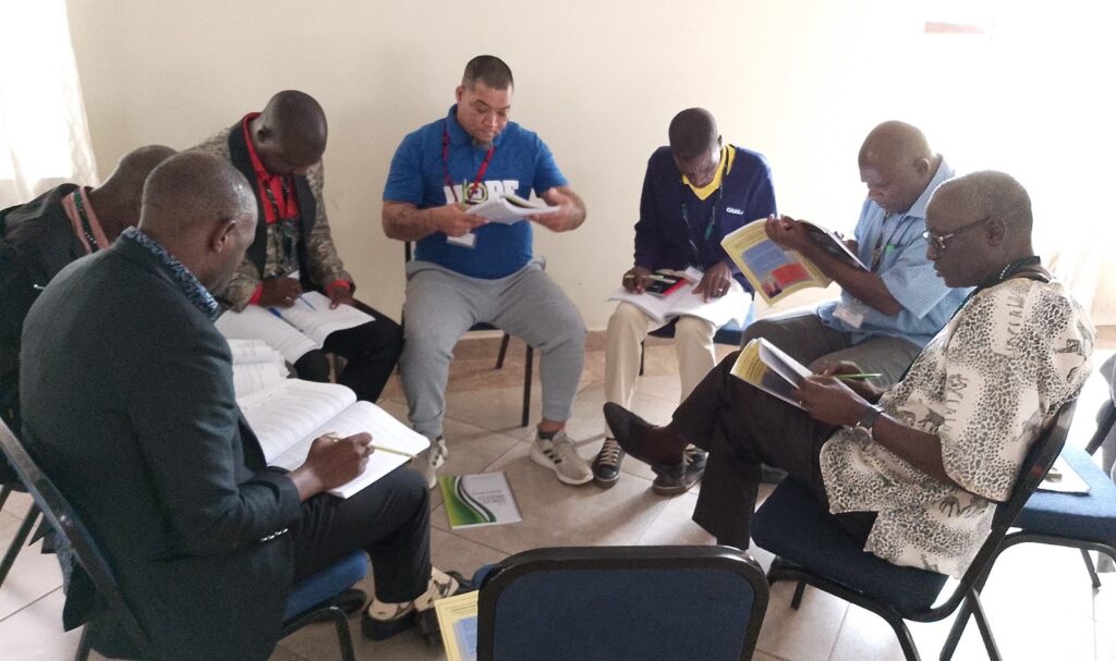Group of men sitting in a circle reading.